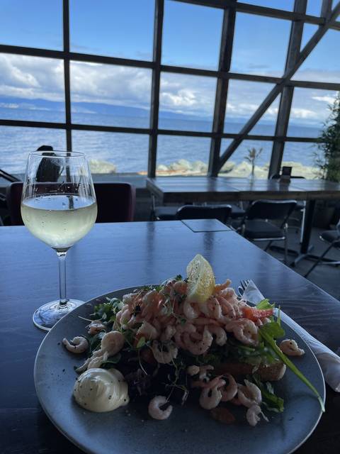 Seafood salad and wine on a table inside a restaurant with a sea view.