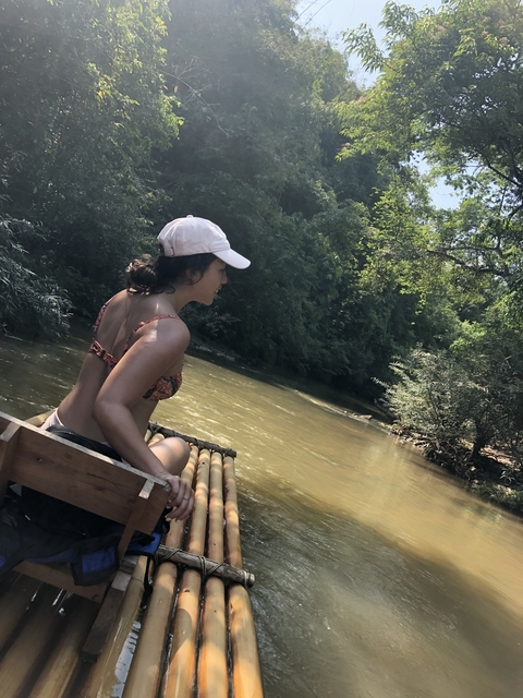 Woman on a bamboo raft in a river surrounded by lush greenery.
