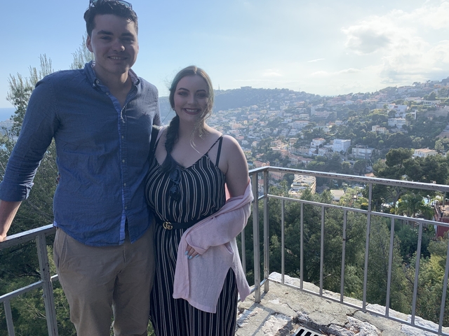 Couple on a balcony with a panoramic view of a city and hills.