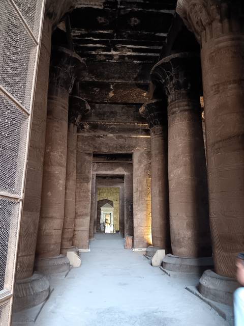 Ancient pillars with hieroglyphs and a person walking through the corridor.