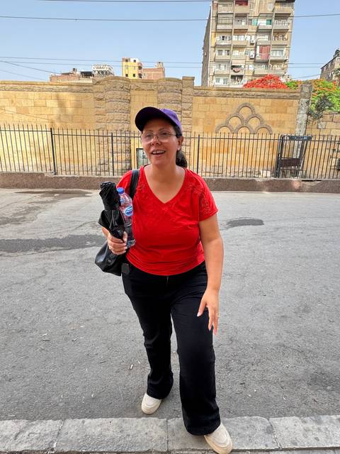 A woman in a red shirt and black pants standing on a paved street.