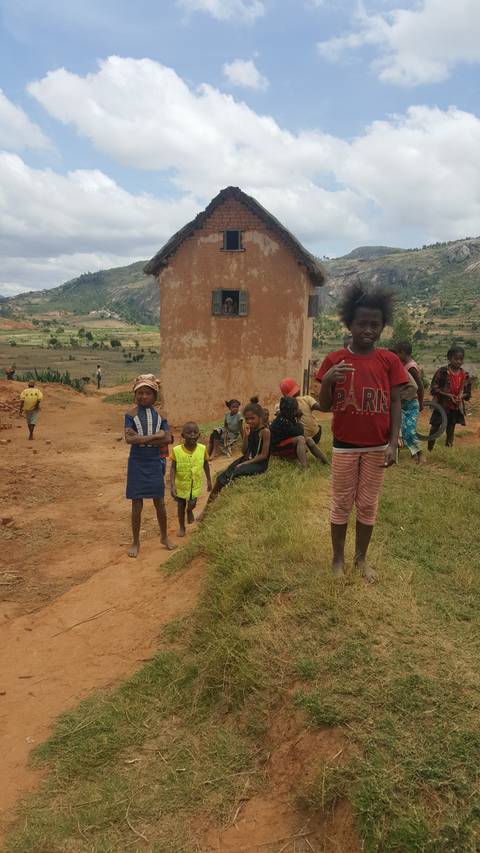       Group of children standing in front of a small building in a rural area.
  