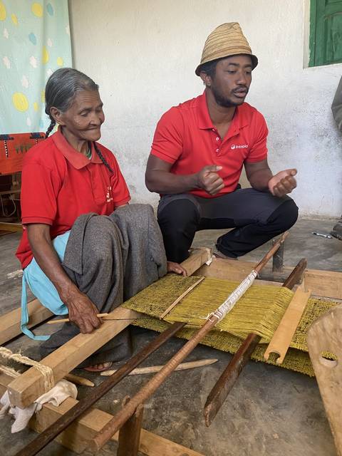       Two people weaving with traditional tools.
  