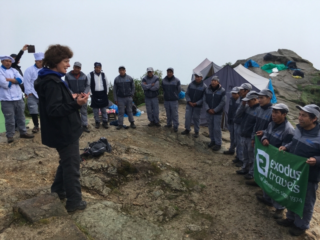 Group of people gathered around a speaker in an outdoor setting.