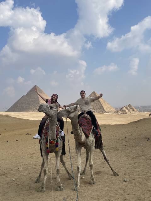       People riding camels near pyramids in Egypt.
  