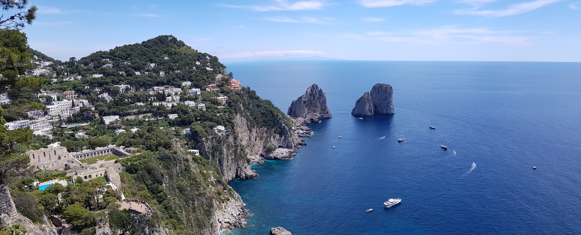 Cliffs and rock formations by the sea with a few boats visible.