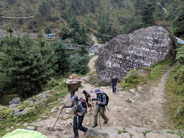 Hikers walking on a trail with a large boulder covered with inscriptions.