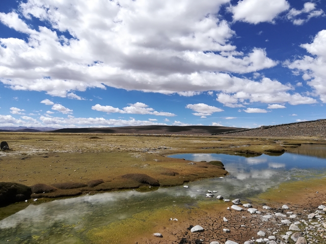 A vast landscape with a small pond and cloud-filled sky.