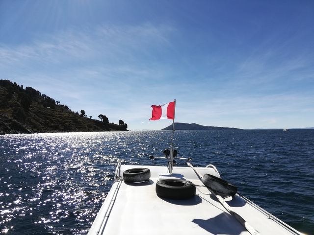       A boat with a Peruvian flag on a lake under a clear sky.
  