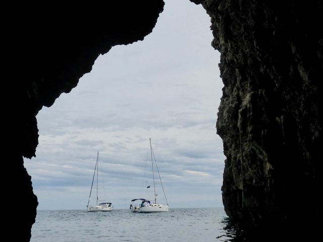View from inside a cave with the sea and sailboats visible.
