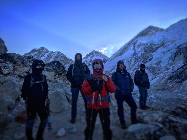       Trekkers standing on a rocky mountain path with snow-covered peaks.
  