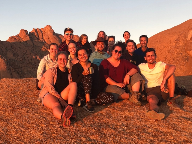 A group of people sitting on a rock during sunset.