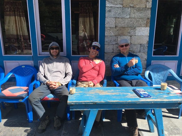       Three people sitting at a table outside a stone building.
  