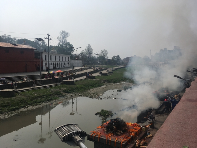       A riverbank with smoke rising from cremation ceremonies.
  