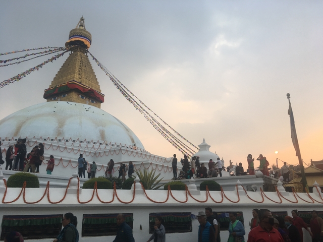       A large stupa surrounded by people, during sunset.
  