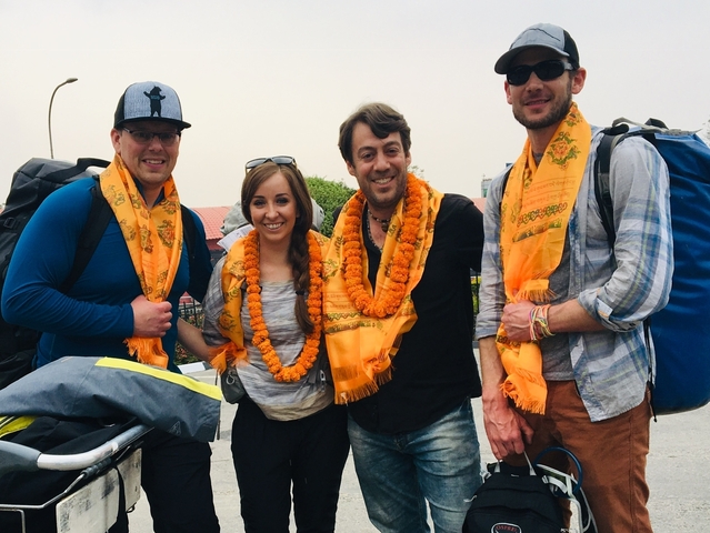       Four people wearing garlands, smiling and posing together.
  