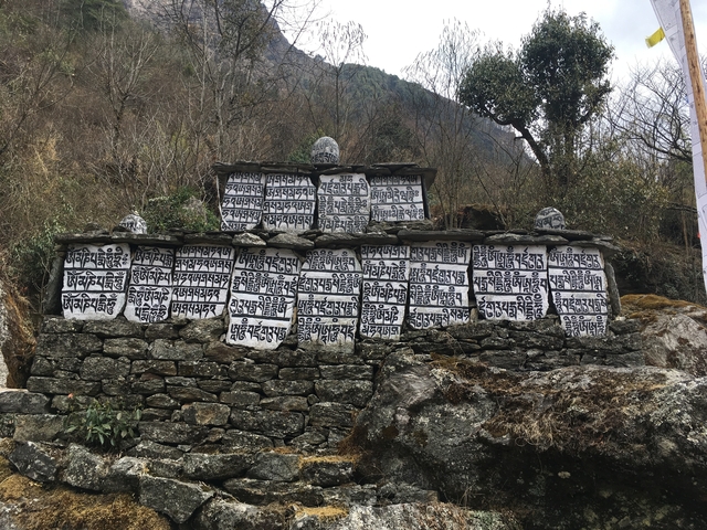       A mani wall with Tibetan inscriptions in a mountainous setting.
  