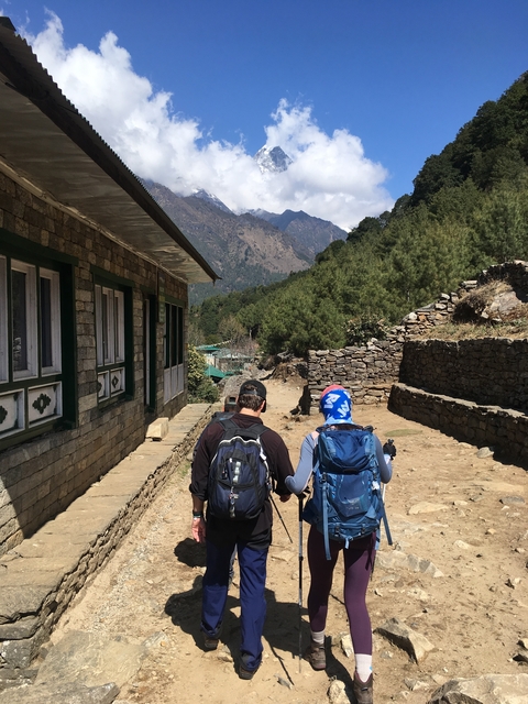       Two trekkers walking along a dirt path in a mountainous area.
  