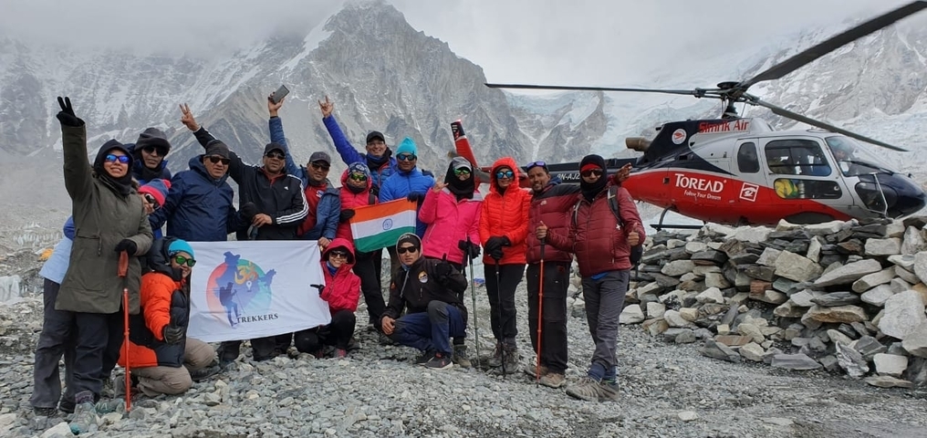       Group of people posing with a helicopter and snowy mountain in the background.
  