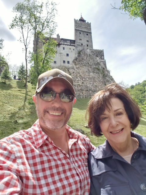 Couple posing in front of a rocky hill with a building.