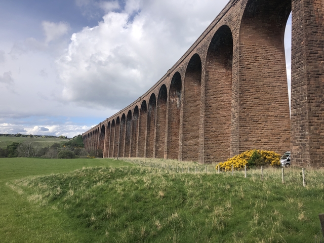Arched stone viaduct in a grassy landscape.