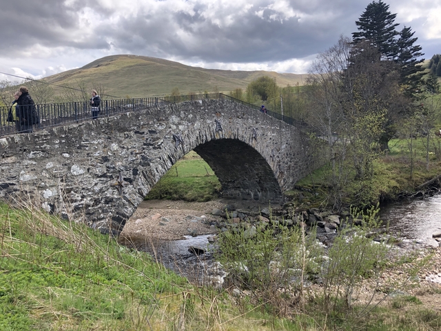       Stone bridge over a river with hilly backdrop.
  