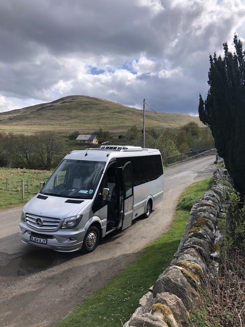 Tour bus on a rural road with hills in the background.