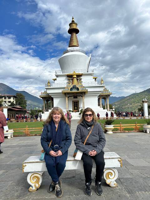       Two people sitting in front of a white stupa
  