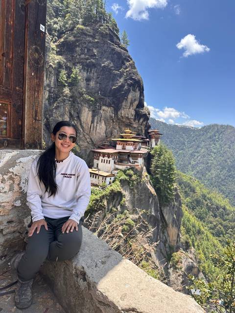 Person sitting on a ledge near a cliffside monastery.