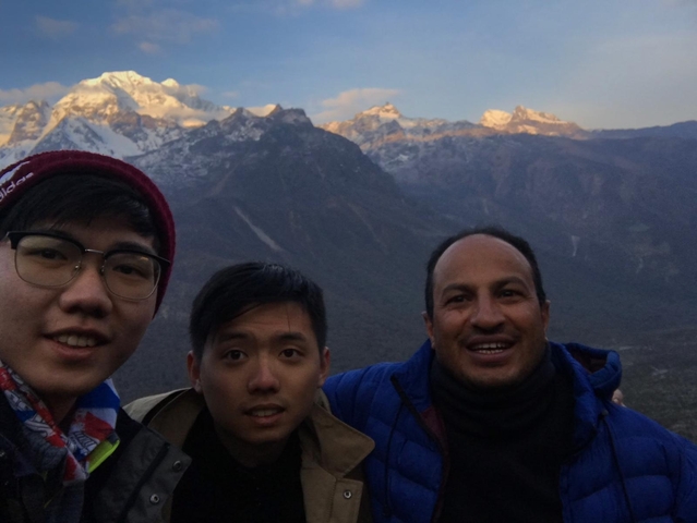 Three people in front of snowcapped mountains at sunset.