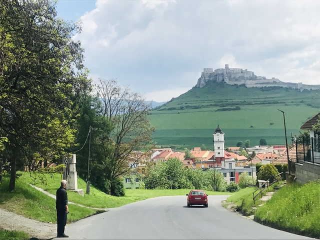 A scenic view of a red car on a road with a castle on a hill in the background.