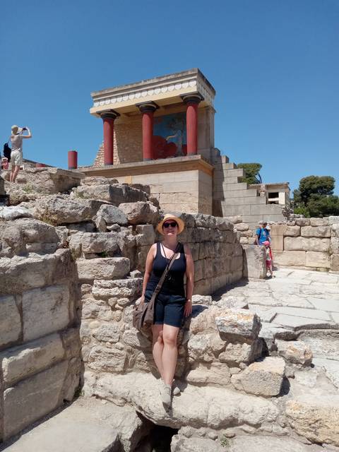       Person standing among ancient ruins with red columns.
  