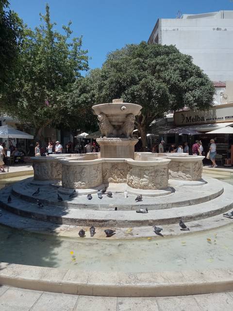       Stone fountain in a city square with pigeons.
  