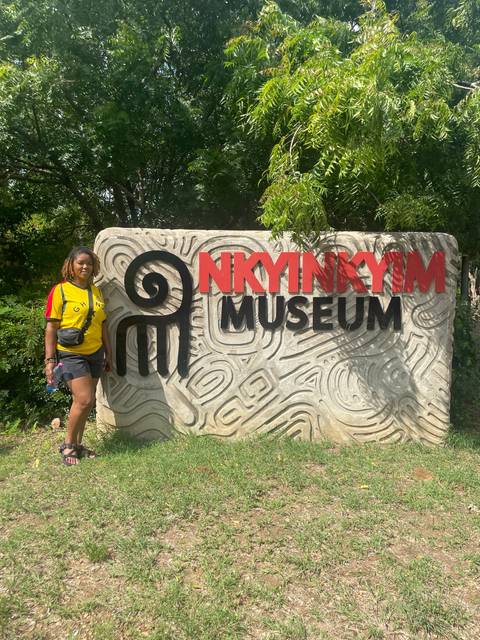       Woman standing by Nkyinkyim Museum sign.
  