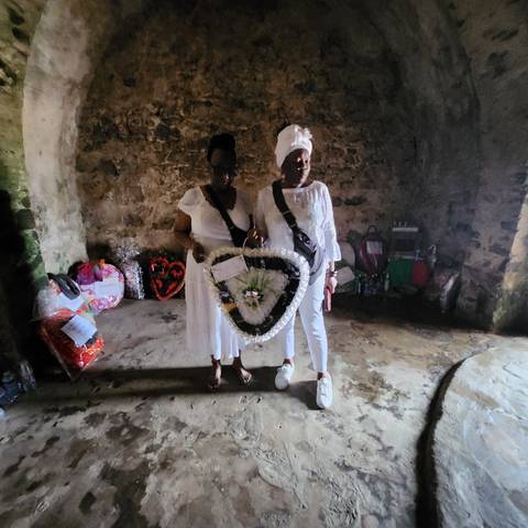       Two people in white clothing holding a floral wreath.
  