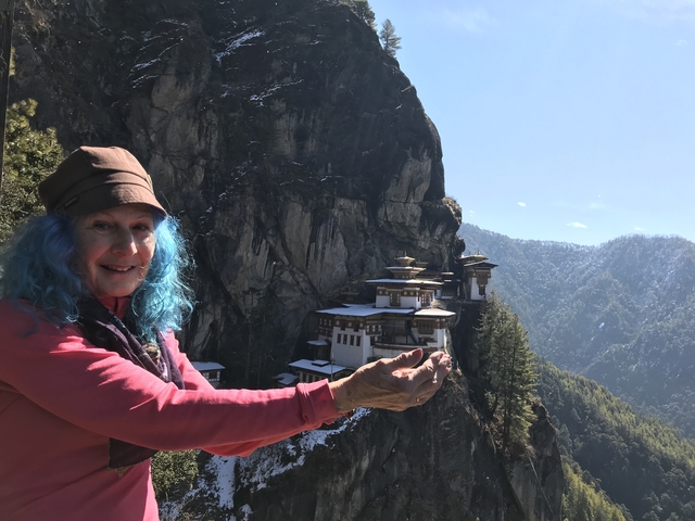 Person posing with hands open towards Taktsang (Tiger's Nest) Monastery on a cliff.