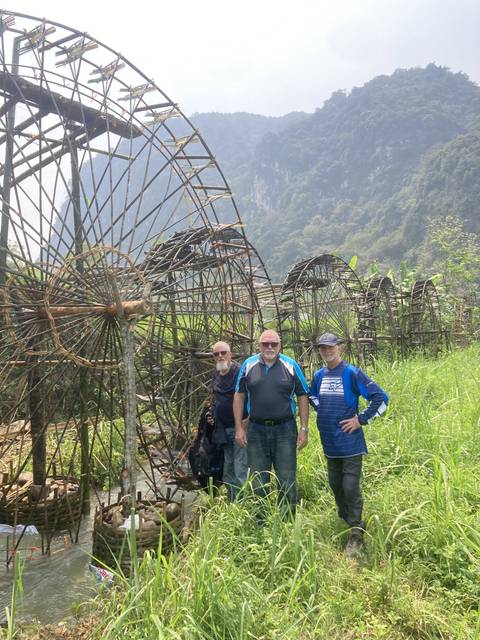       Three people posing near wooden waterwheels
  