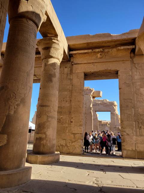 Ancient Egyptian temple ruins with tourists exploring, columns visible.