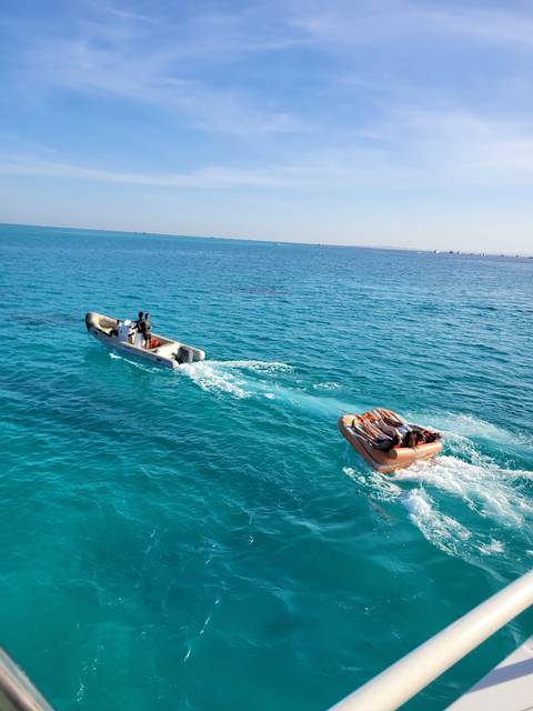 People riding small boats on the ocean, bright sunny day.