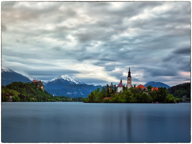 Wide view of Lake Bled with a church on the island and mountains in the background.
