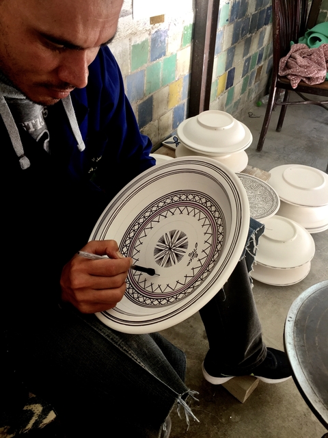       Person painting intricate designs on a ceramic plate.
  