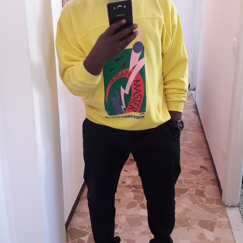       Person standing in a hallway, wearing a brightly colored sweatshirt.
  