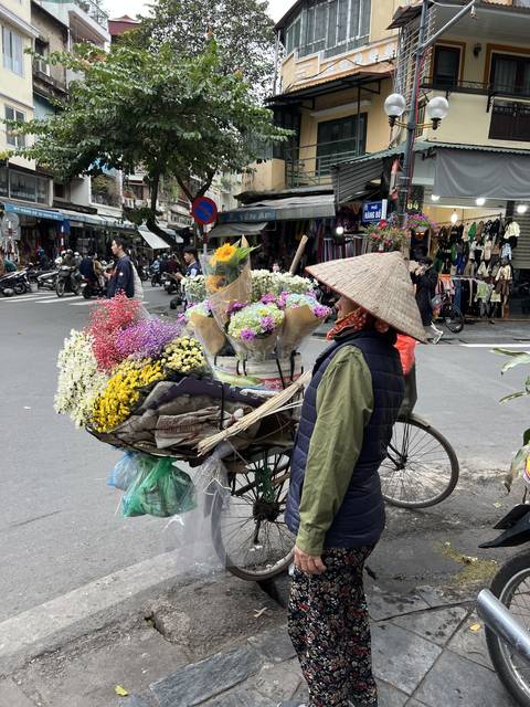       Person with conical hat next to a bicycle carrying flowers.
  