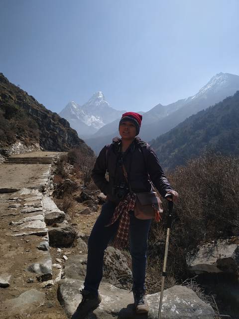 Person posing with trekking poles on a mountain trail.