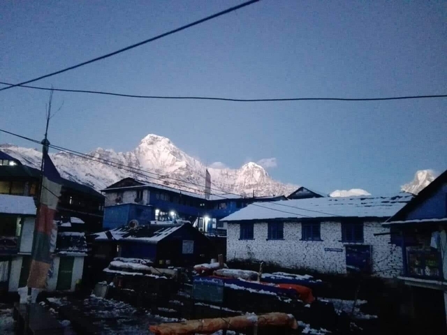 Snow-covered mountains behind village houses at dusk.