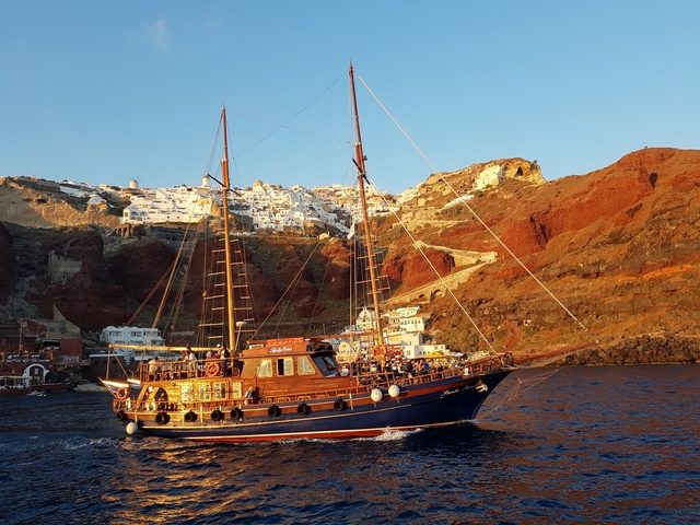 Sailing ship at sea with a backdrop of a hillside town.