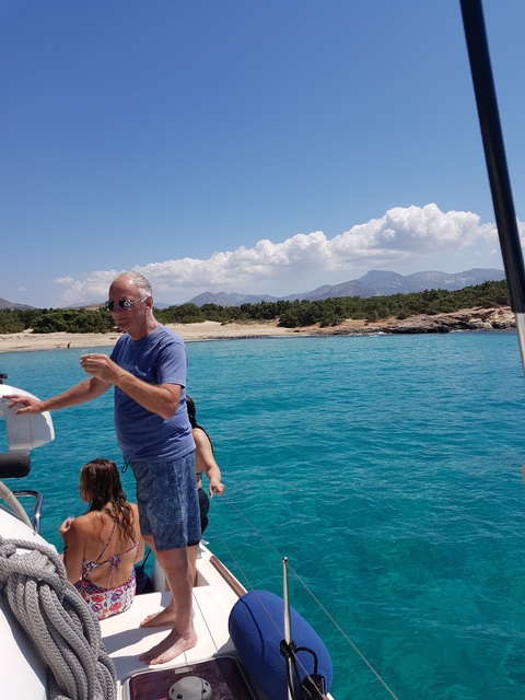 Man standing on a boat near a turquoise sea and distant mountains.