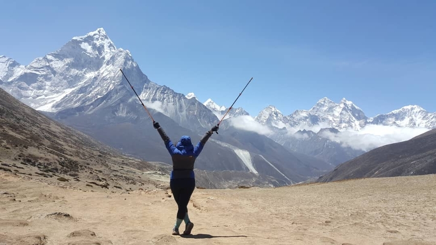 Person with trekking poles raised in front of mountains.