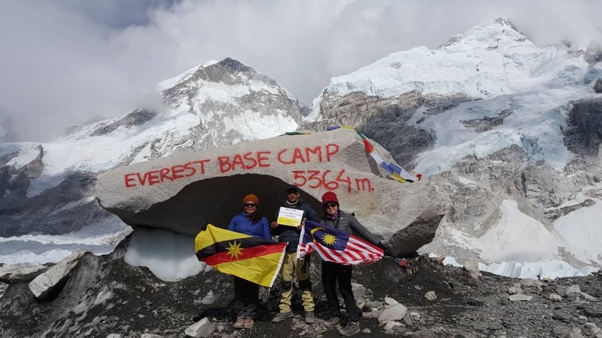People with flags at Everest Base Camp with snowy mountains.
