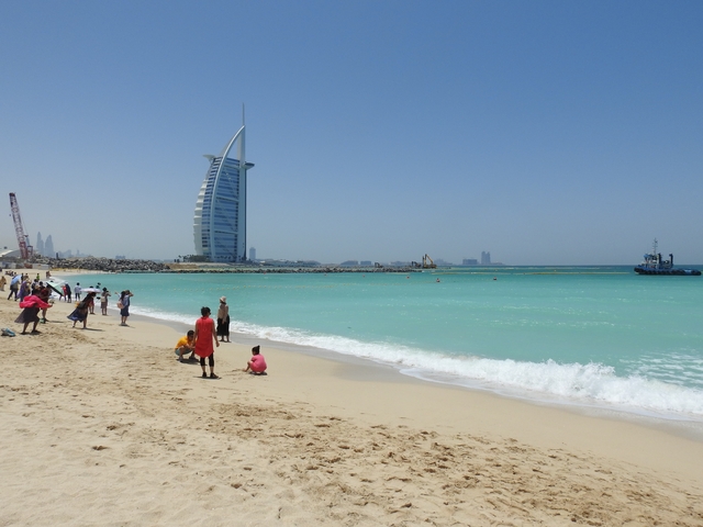 People enjoying a beach with the Burj Al Arab in the background.